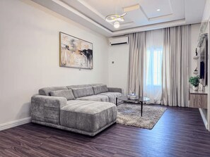 A modern living room with a sectional sofa, a coffee table, and a large abstract painting on the wall. - Stylish 1-Bedroom Apartment in Lekki 1 with Fast Wi-Fi & 24/7 Power (Lagos)