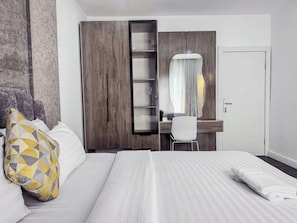 A hotel room with a bed, a desk, a chair, and a wardrobe. - Stylish 1-Bedroom Apartment in Lekki 1 with Fast Wi-Fi & 24/7 Power (Lagos)