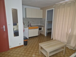 A compact kitchen with a sink, microwave, and cabinets. There's a small table and a trash bin. - Studio apartment with a bathroom, 150 meters from the beach (Agde)