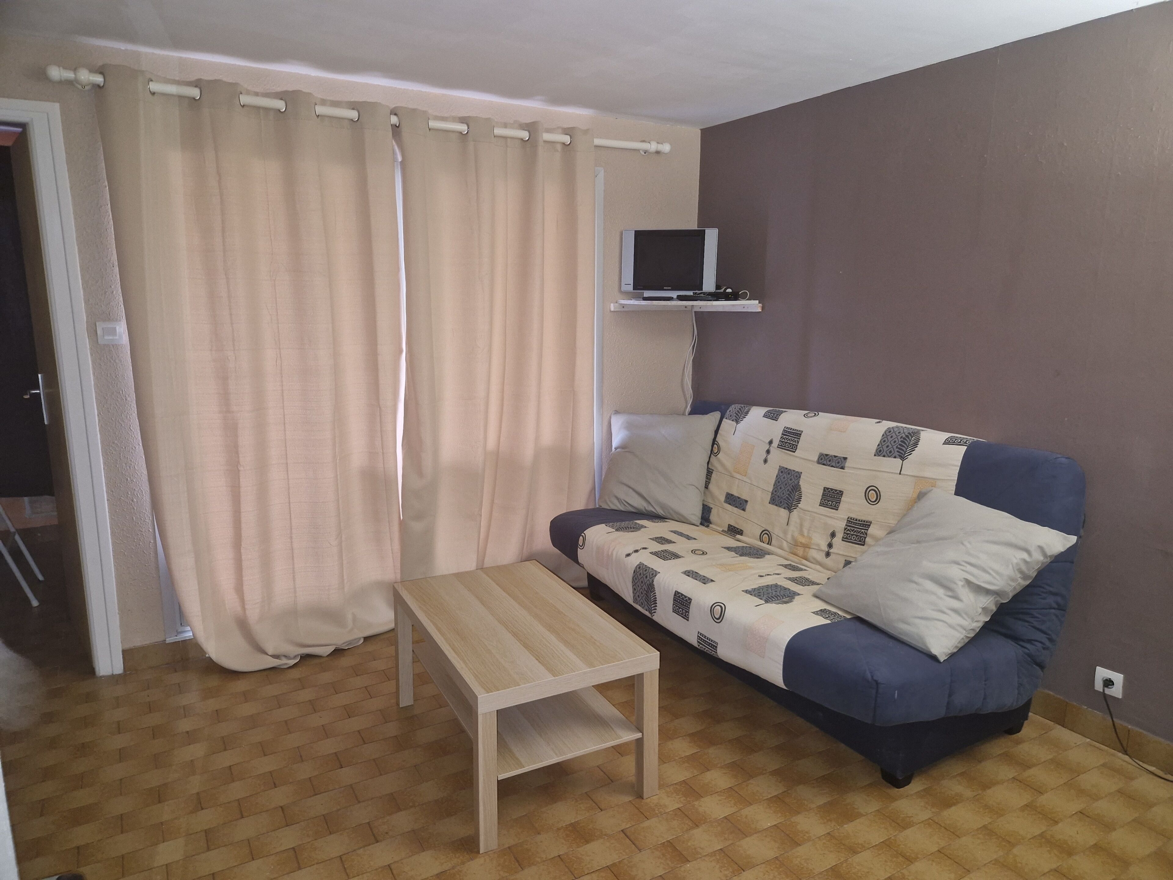 A living room with a sofa, a small table, a television on a stand, and a curtain.