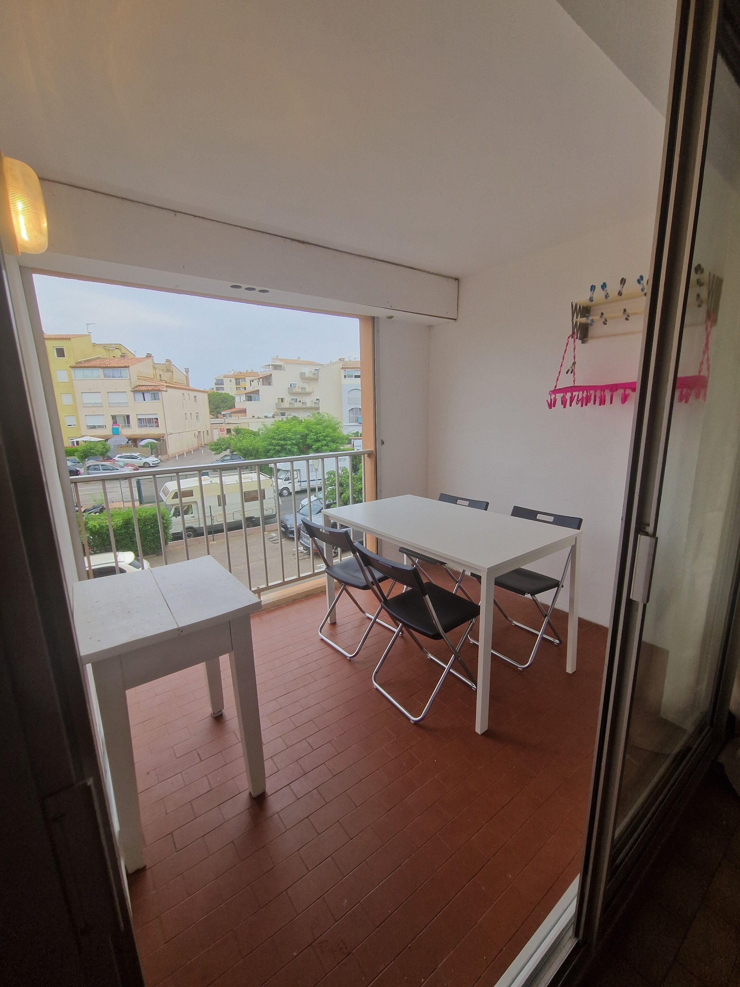 Een balkon met een tafel, stoelen, een glazen deur en uitzicht op gebouwen en groen.