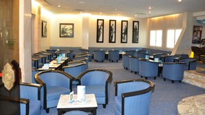 A hotel lobby with rows of seating, framed artwork on the walls, and a large window allowing natural light.