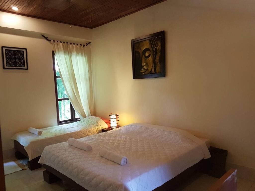 A hotel room with two beds, a window with curtains, a wall-mounted painting, and a bedside lamp.