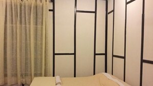 A single bed with a beige bedspread and white pillows, a curtain, and a wall with a simple, geometric pattern.