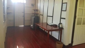 A hallway with a wooden floor, a table with a kettle, and a door with a window.