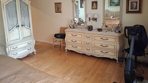 Ein Zimmer mit großem Schrank, Schminktisch mit Spiegeln, Stuhl und Staubsauger.