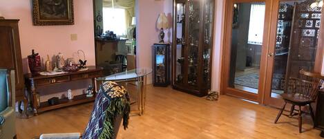 A living room with a wooden floor, a patterned armchair, a glass-top coffee table, a ceiling fan, and a door leading to a balcony.