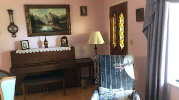 A living room with a piano, a chair, a lamp, and a painting on the wall.