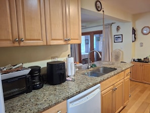 A kitchen with wooden cabinets, a granite countertop, a coffee maker, a dishwasher, and a sink.