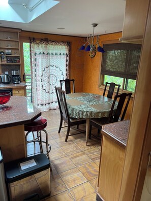 Un comedor con una mesa redonda, seis sillas, una araña y una ventana con vista a la vegetación.