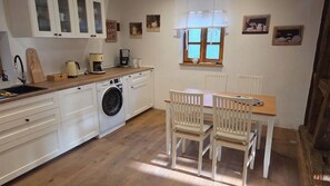 Una cocina funcional con lavadora, una mesa de comedor con sillas y un ventanal con cortinas.