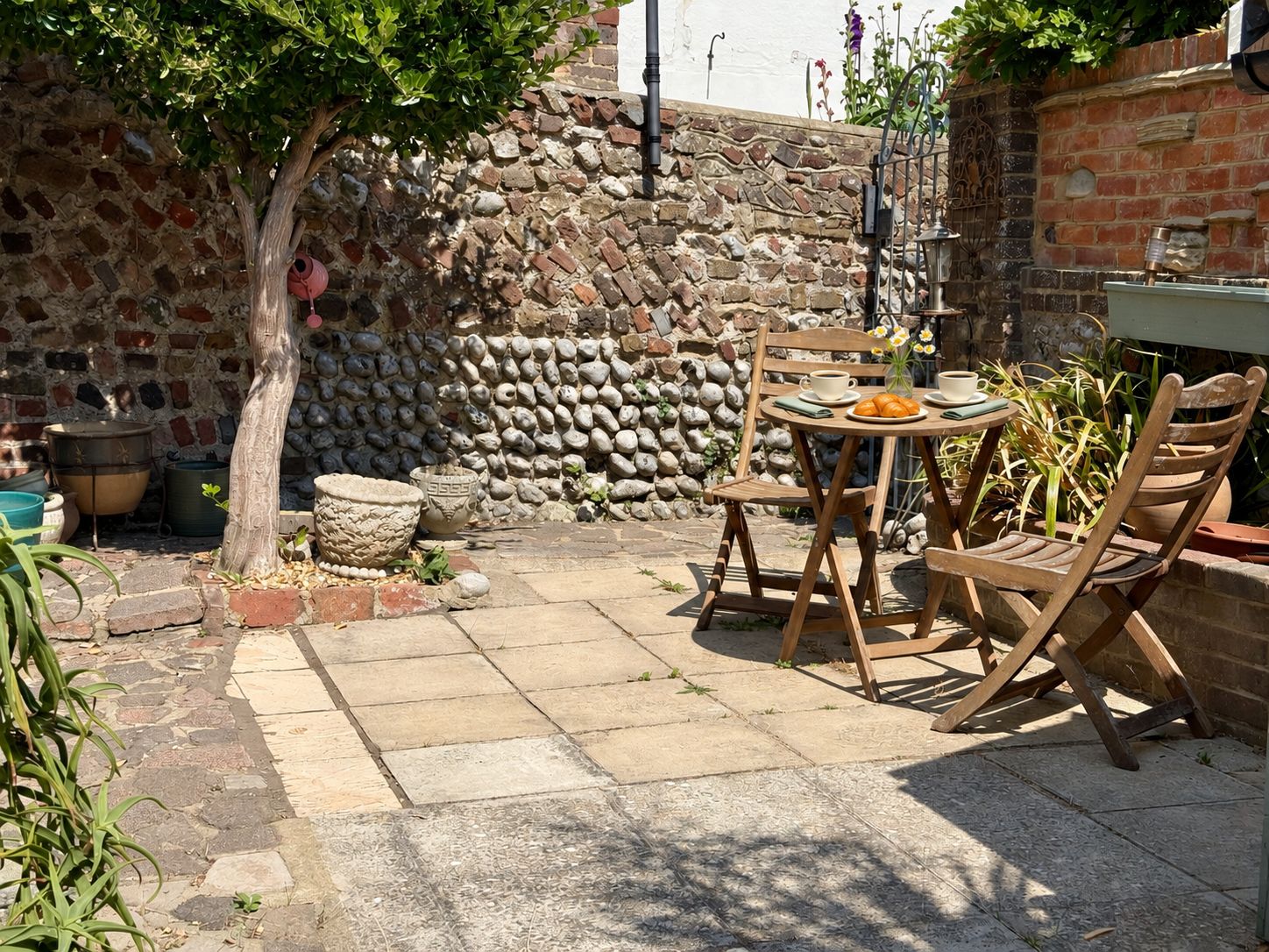 Un patio con un muro de piedra, un árbol y una mesa con sillas.