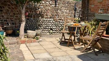 Un patio con un muro de piedra, un árbol y una mesa con sillas.