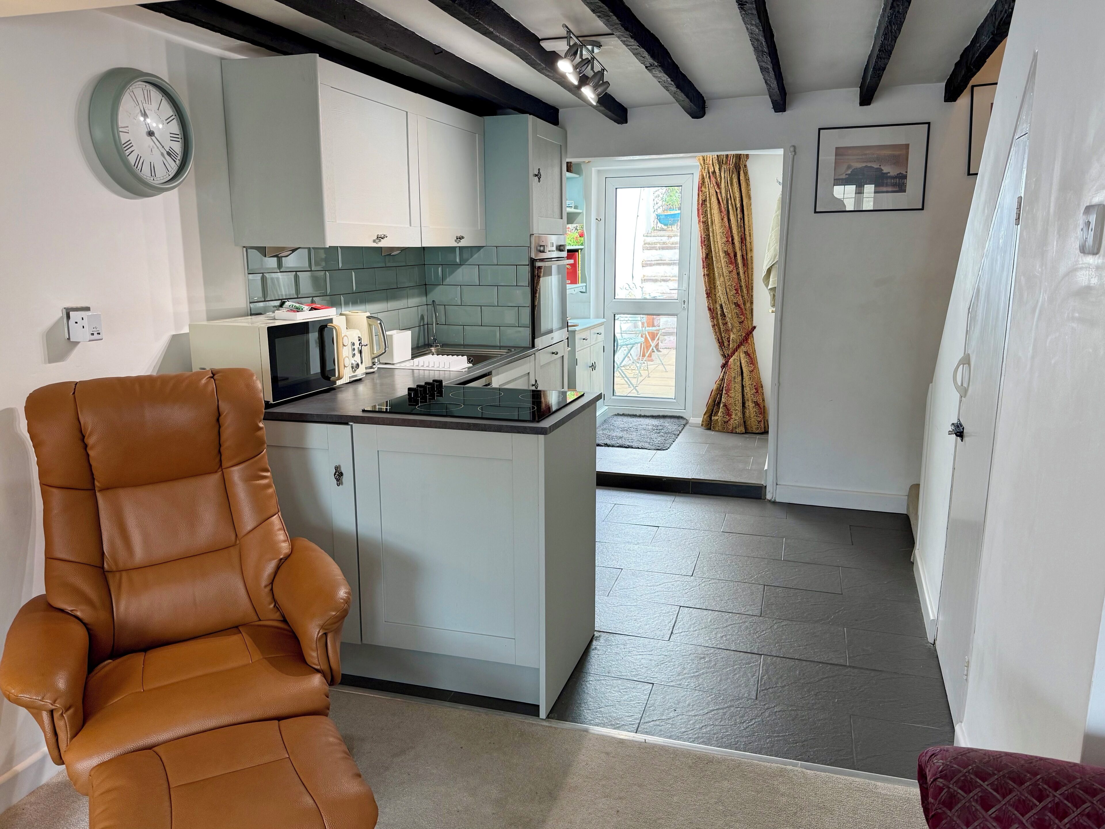 A modern kitchen with a built-in island, a brown leather chair, and a dining area with a patterned curtain.