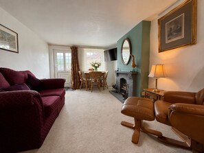 Una sala de estar con sofá, una silla, chimenea, televisor y un comedor con mesa y sillas.
