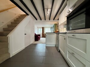 A modern kitchen with a built-in oven and cabinets, a staircase leading to another room, and a view of a living area with a couch and curtains.
