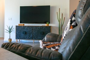 A living room with a leather sofa, a flat-screen TV mounted on the wall, a decorative cabinet, and a cactus plant. - Star Light, Estrella Mountain Ranch (Goodyear)