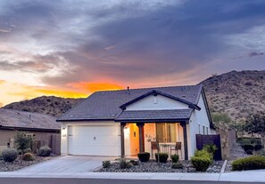 A single-story house with a garage, surrounded by desert vegetation, under a sunset sky. - Star Light, Estrella Mountain Ranch (Goodyear)