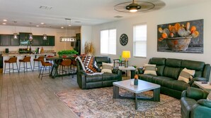 A modern living room with a green sofa, a coffee table, and a dining area with chairs and a table. - Star Light, Estrella Mountain Ranch (Goodyear)