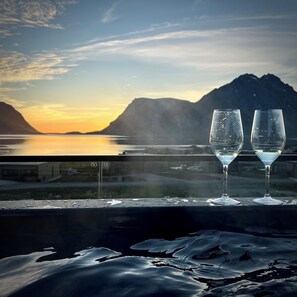 Two glasses on a reflective surface with a view of a mountainous landscape and a body of water.