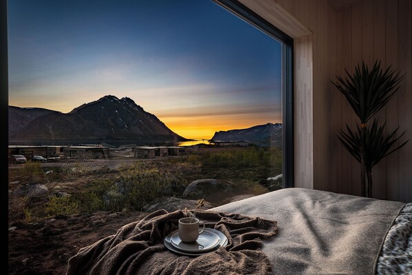 A room with a large window overlooking a mountainous landscape at sunset.