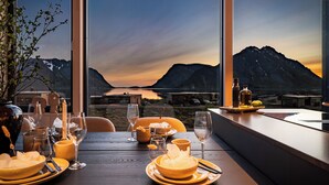 A dining table set for two with a view of mountains and a lake.