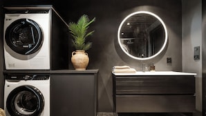 A modern bathroom with a washing machine, a potted plant, a round mirror, and a sink with towels.