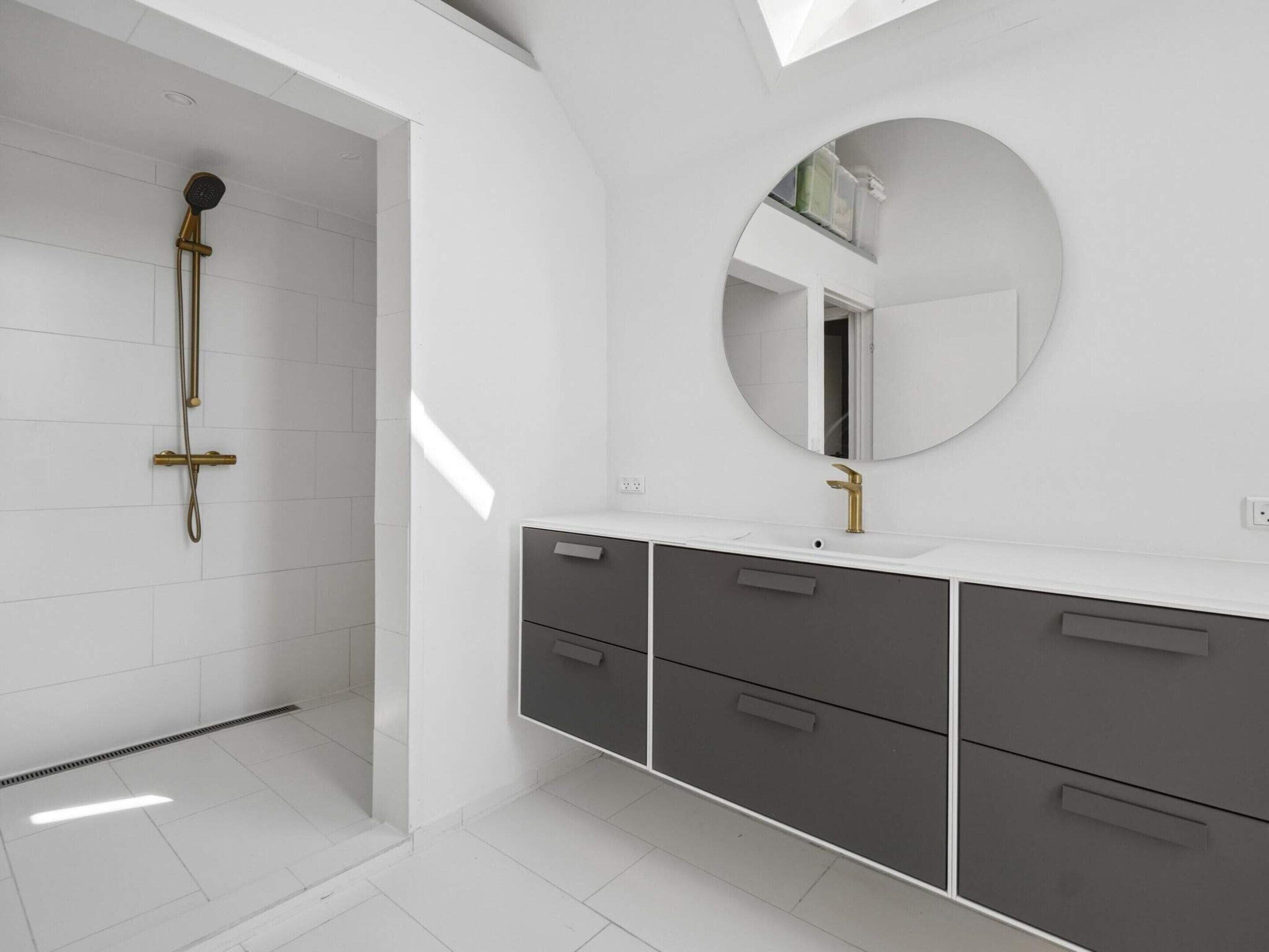 A modern bathroom with a shower, a sink with a gold faucet, and a large mirror.