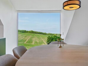 Ein Essbereich mit Blick auf ein grünes Feld durch ein großes Fenster, ein runder Tisch und eine hängende Leuchte.