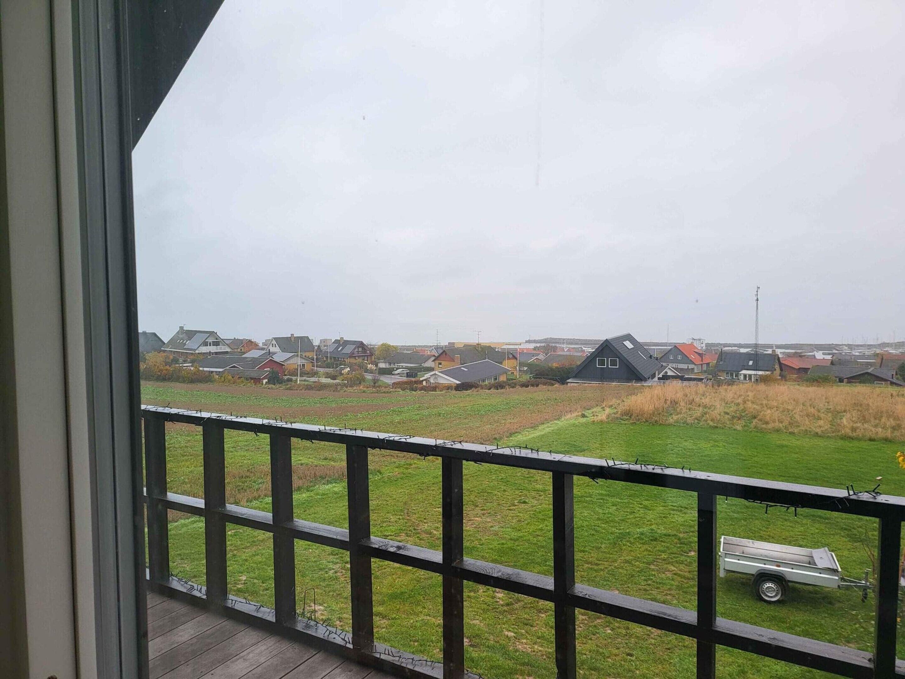 Vista de uma varanda com guarda-corpo de madeira, com vista para uma área residencial com casas e um campo gramado.