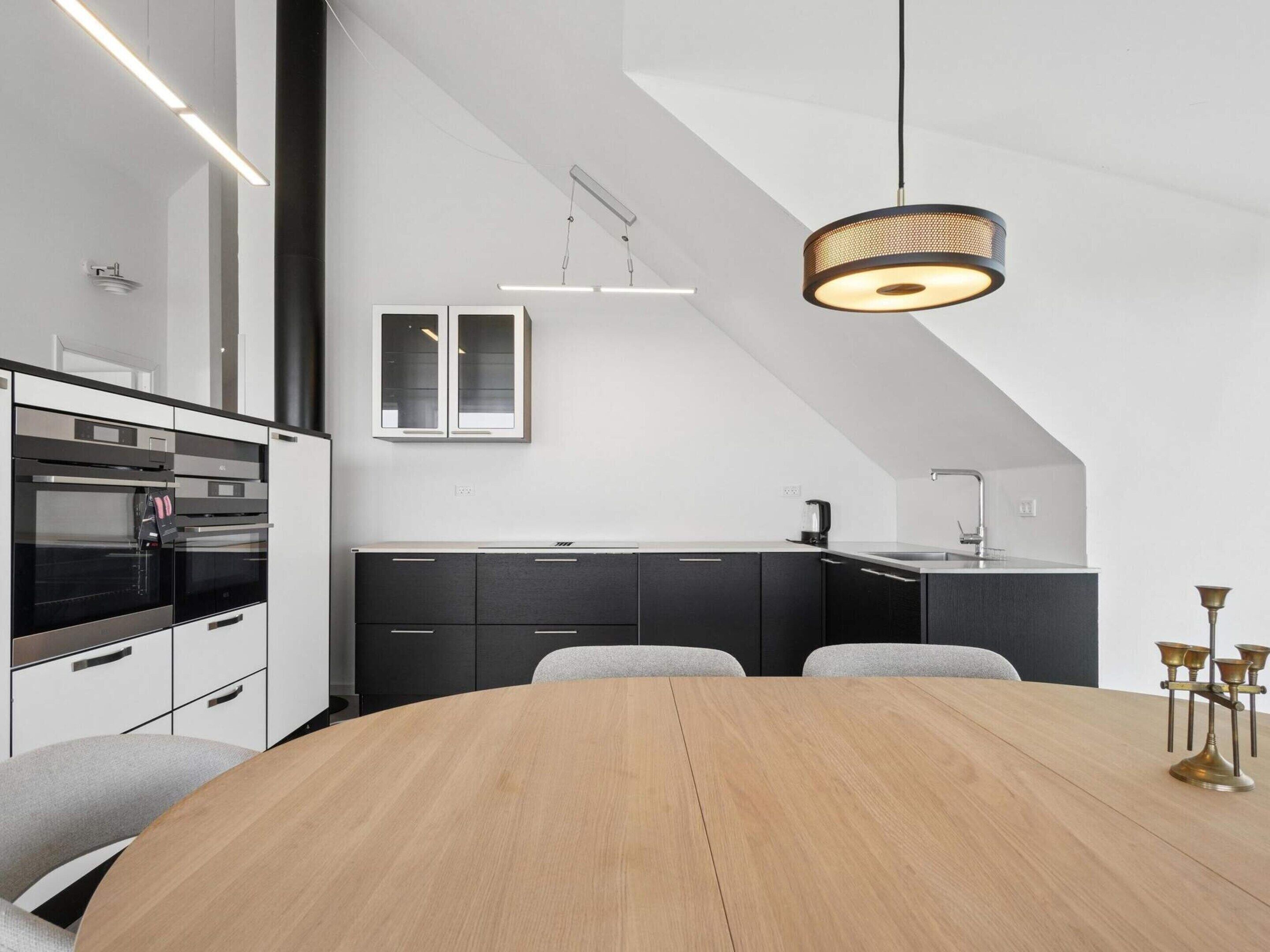 Een moderne keuken met een houten eettafel, zwarte kastjes en roestvrijstalen apparatuur.