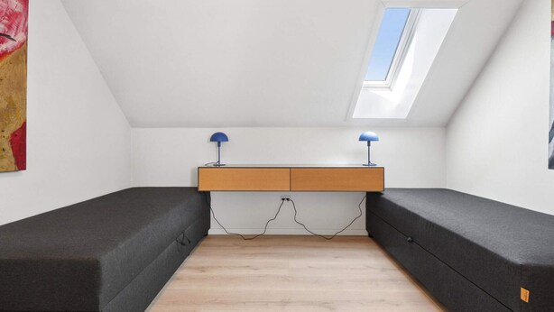 A room with a sloped ceiling, a skylight, a wooden desk with two lamps, and two dark sofas. - 4 Star Holiday Home in Allinge (Allinge)
