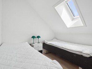 Ein Zimmer mit zwei Betten, einem kleinen weißen Nachttisch und einem Oberlicht.