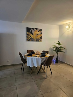 A dining area with a round table set for four, a potted plant, and a wall-mounted light fixture. - Un T2 récent  , confortable  dans un petit  immeuble au coeur de Saint Denis (Saint-Denis)