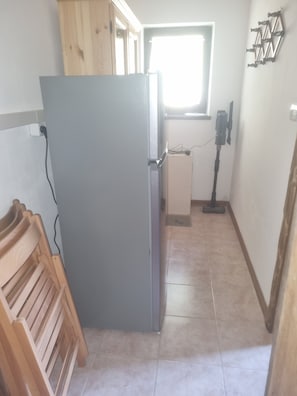 Une cuisine de taille réduite, équipée d’un réfrigérateur, de meubles en bois, d’une fenêtre et d’un aspirateur.