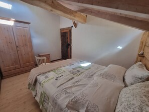 Une chambre avec un plafond en bois, un lit recouvert d’une literie à motifs floraux, une armoire en bois et une petite table de chevet.