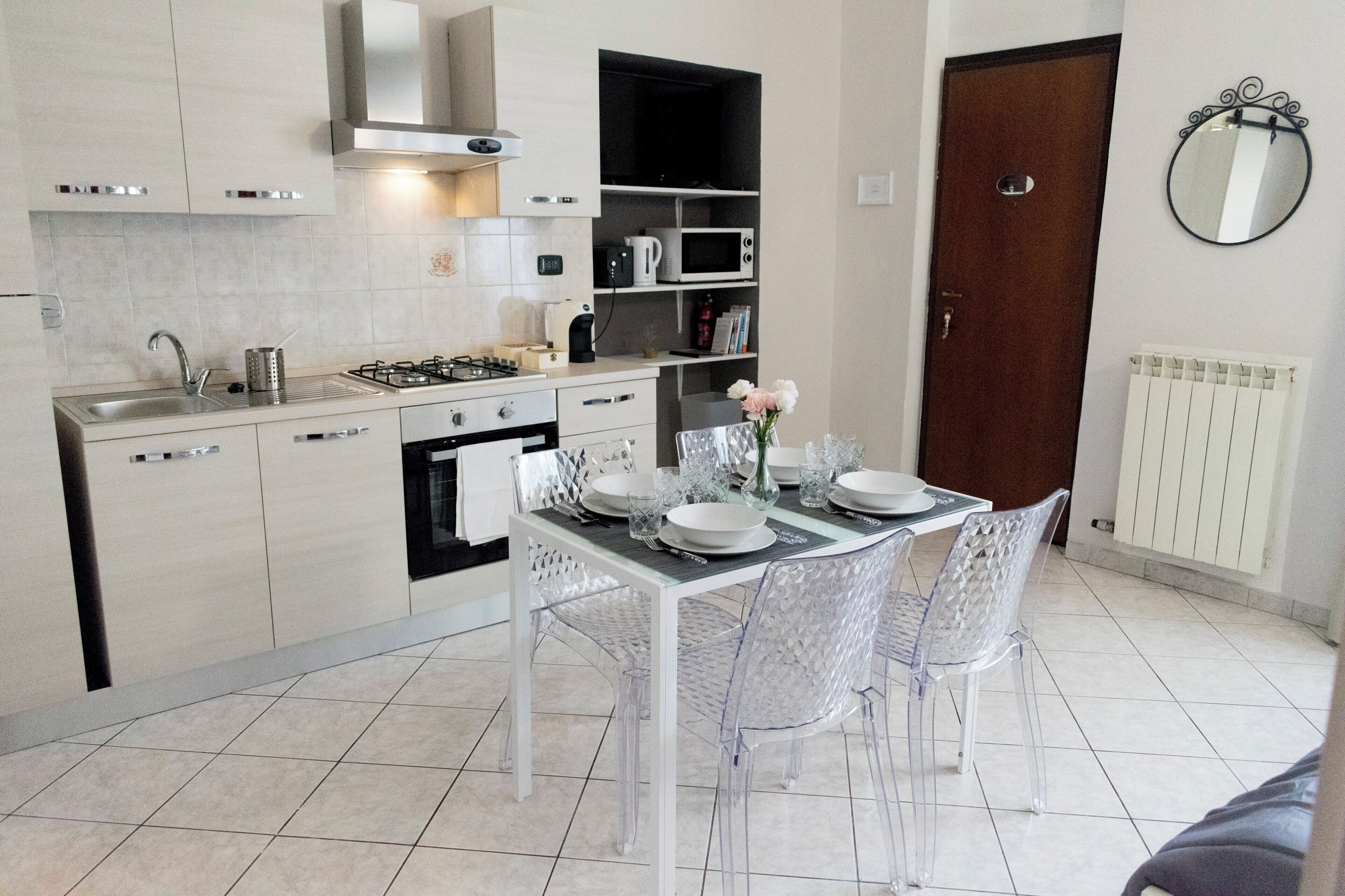 Una cucina moderna con piano cottura a gas, lavello e forno a microonde. È presente un tavolo da pranzo con sedie e un vaso di fiori.