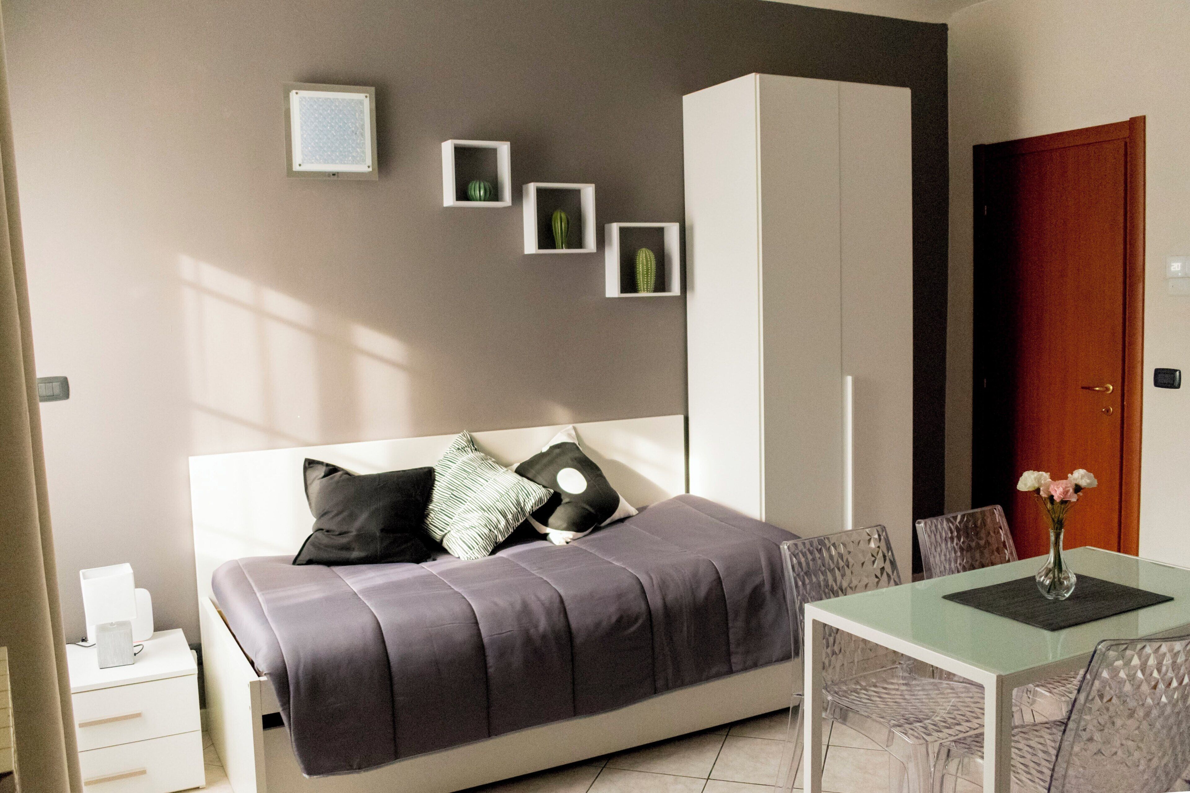 Una camera da letto con un letto, comodini, un armadio, una scrivania con sedie e una porta.