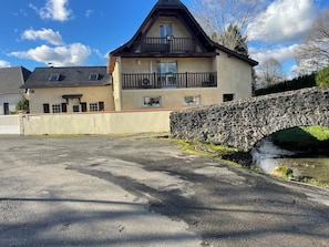 Ein zweigeschossiges Gebäude mit einer Stegbrücke über einem Wasserkanal, einer Schotterauffahrt und einem weißen Zaun.