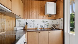 A kitchen with wooden cabinets, a white countertop, a built-in oven, a sink, and a window with a view of greenery. - 5 Star Holiday Home in Brenderup Fyn (Middelfart)
