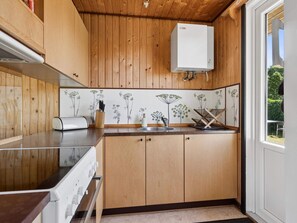 Eine Küche mit Holdekor, einer weißen Arbeitsplatte, einem eingebauten Ofen, einer Spüle und einem Fenster mit Blick auf Grünflächen.