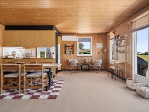 Eine moderne Küche mit Holzschränken, eine Essecke mit kariertem Teppich und ein Sitzbereich mit Blick.