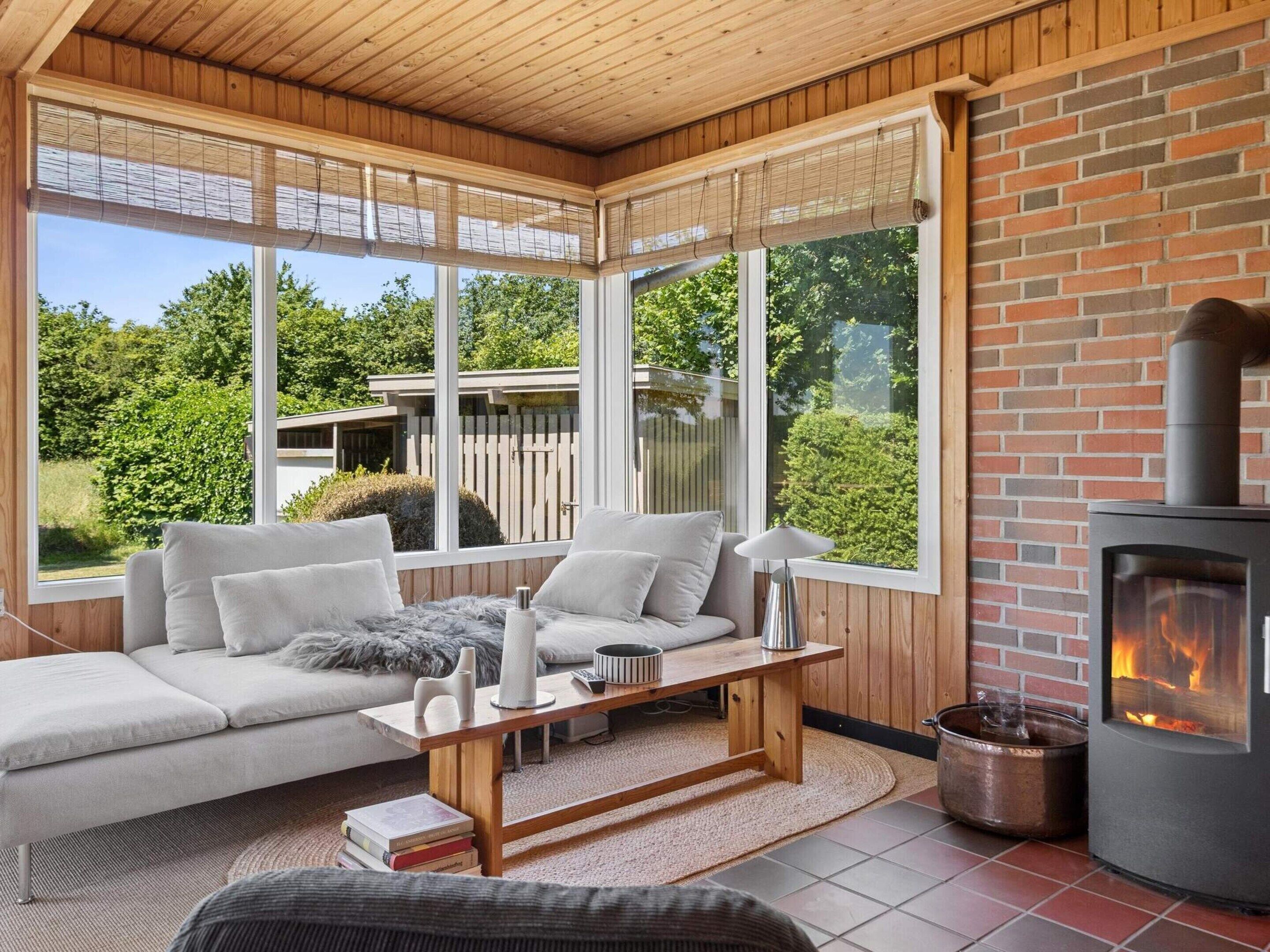 Un cuarto acogedor con chimenea, un sofá, una mesa y ventanas amplias que dan al exterior.
