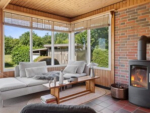Un cuarto acogedor con chimenea, un sofá, una mesa y ventanas amplias que dan al exterior.