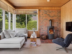 A cozy living room with a sofa, a chair, a fireplace, and a TV mounted on the wall. - 5 Star Holiday Home in Brenderup Fyn (Middelfart)