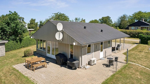 A single-story house with a covered patio area, satellite dishes, and outdoor furniture. - 5 Star Holiday Home in Brenderup Fyn (Middelfart)