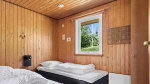 A room with wooden walls, two beds with white bedding, a window with a view of greenery, and a wall-mounted light fixture. - 5 Star Holiday Home in Brenderup Fyn (Middelfart)