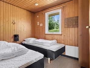 Ein Zimmer mit Holzwänden, zwei Betten mit weißer Bettwäsche, einem Fenster mit Blick auf Grünflächen und einer Wandleuchte.