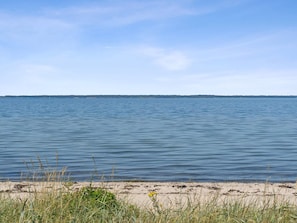 Ruhige Wasseroberfläche mit weiter Küste und bewölktem Himmel.