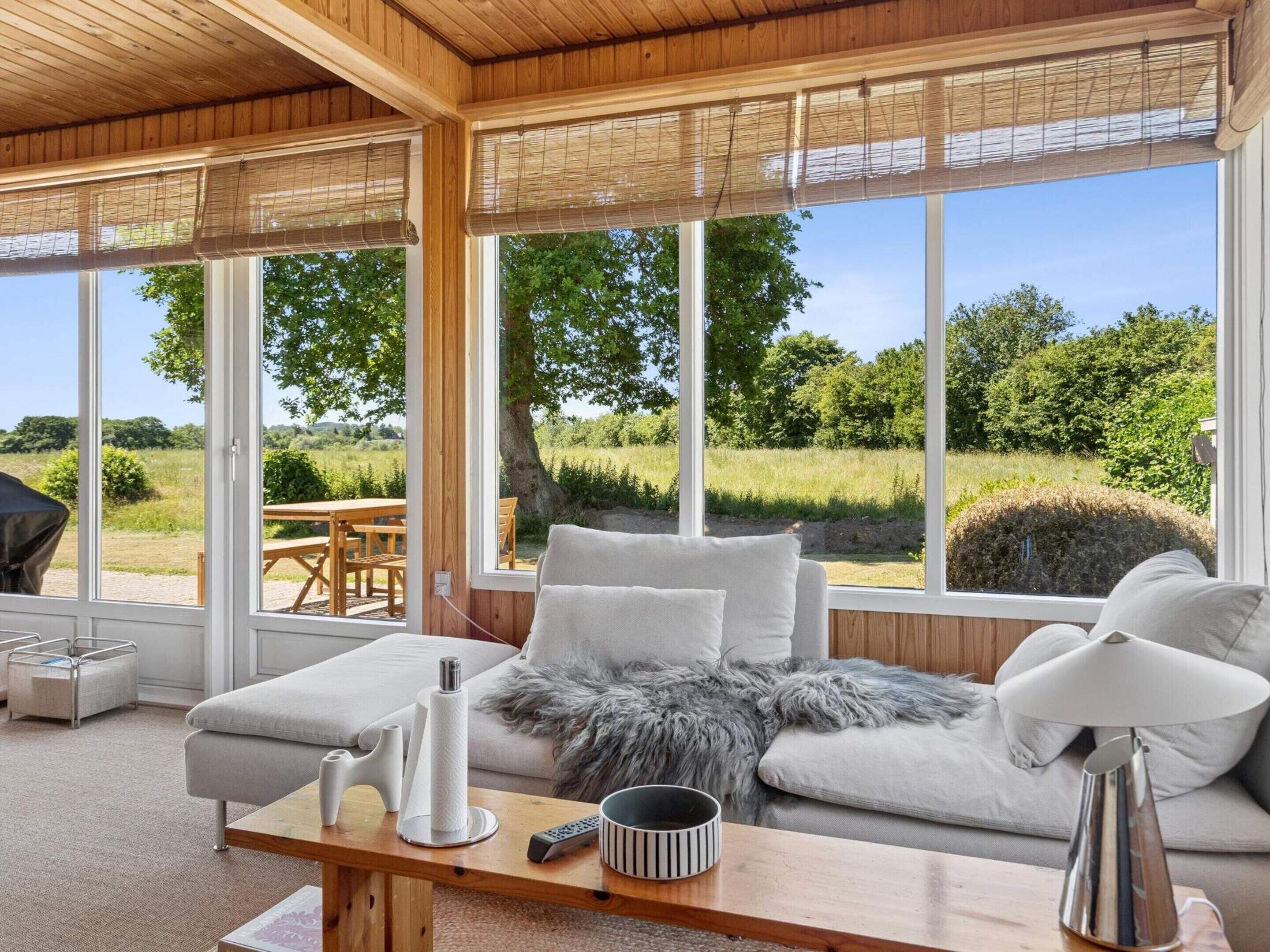 Una sala de estar moderna con un sofá, una mesa de centro y vistas a un jardín a través de amplios ventanales.